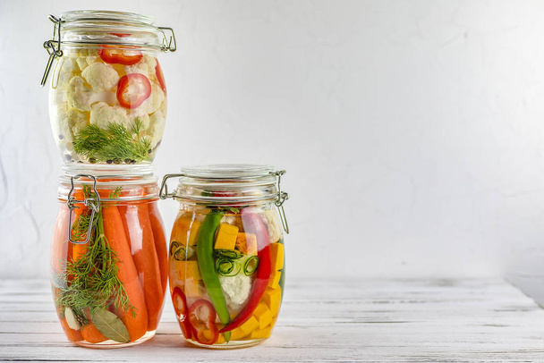 three glass jars of fermented cauliflower,carrots, vegetables on a light background. fermentation is a source of probiotic. copy space - Fotó, kép