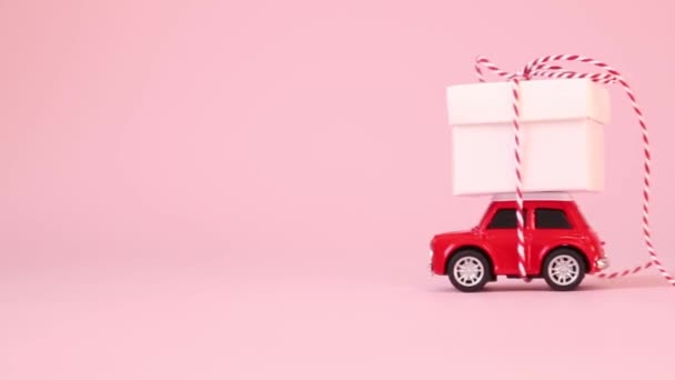 Caja de regalo de entrega de coche de juguete rojo con lazo de cinta sobre un fondo rosa. Cumpleaños, Día de San Valentín, concepto de Día de la Mujer
. - Imágenes, Vídeo