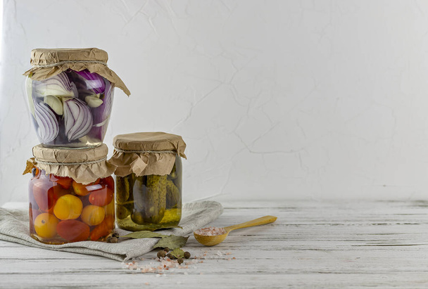 drei Gläser mit fermentierten Gurken, Tomaten, Zwiebeln. Gemüse auf hellem Hintergrund. mit Textilhellgrau. Die Fermentation ist eine Quelle von Probiotika. Kopierraum - Foto, Bild