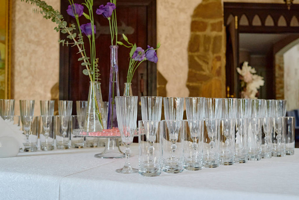 Sprankelend glaswerk en bloemen op de eettafel in restaurant, kopieerruimte. Kristallen glazen klaar voor viering - Foto, afbeelding