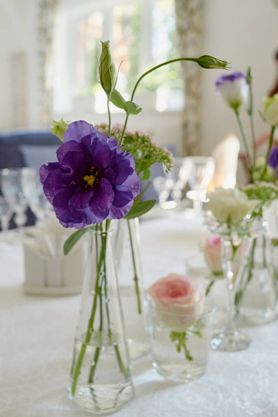 Beautiful floral arrangement on wedding table in restaurant, copy space. Bouquet of pink roses, purple eustoma and greenery in glass vases - Photo, Image
