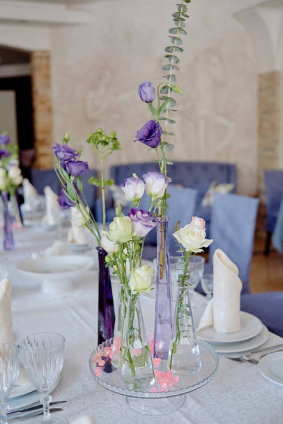 Hermoso arreglo floral en la mesa de la boda en el restaurante, espacio de copia. Ramo de rosas rosadas, eustoma púrpura y vegetación en jarrones de vidrio
. - Foto, imagen