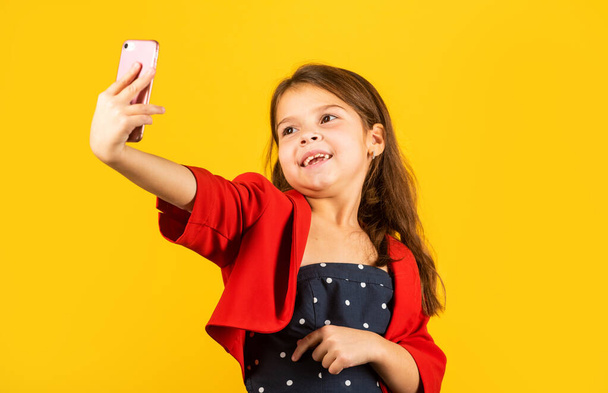 Selfie time. Small girl take selfie with smartphone yellow background. Little child selfie camera in mobile phone. Enjoying selfie session in fashion style. Communication online. Social network - Foto, Imagen