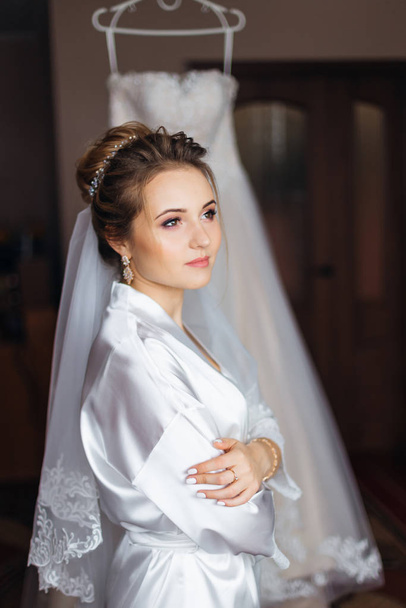 bride in white bathrobe with make up and bridal veil crossed arm - Photo, Image