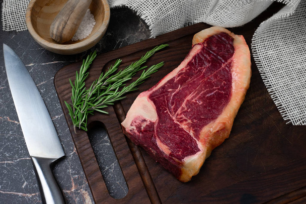Sucho zrající Striploin steak a sůl na tmavé dřevěné desce, rustikální s - Fotografie, Obrázek