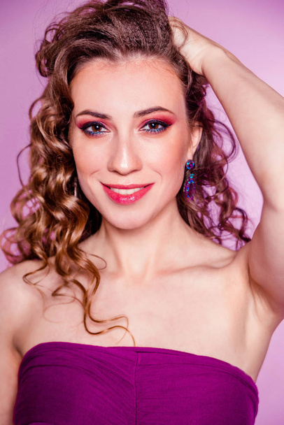 Sensual beautiful brunette girl with red makeup, curly hair and a burgundy top posing on a purple background - Fotó, kép
