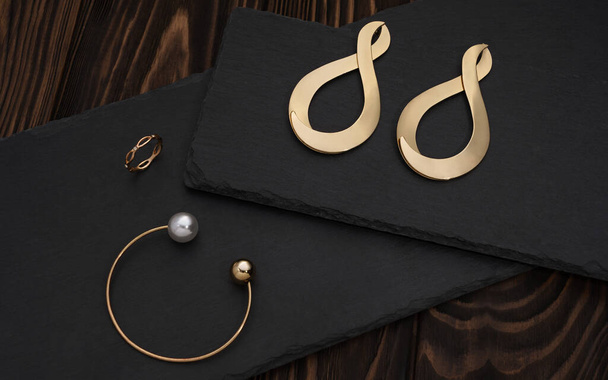 Golden bracelet, ring and infinity symbol shape earrings pair on black plate - Photo, Image