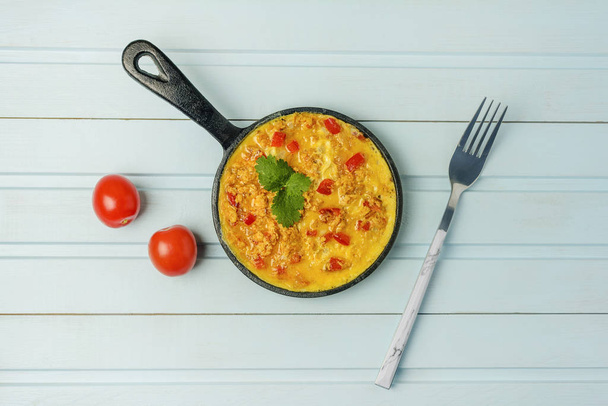 Freshly made omelet from eggs and vegetables. Turkish national recipe Menemen with eggs, bell pepper and tomatoes. Photo on a blue background with copy space - Фото, изображение