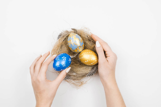 Easter golden decorated eggs in nest with woman hands isolated on white background for web banner. Minimal easter concept. Happy Easter card with copy space for text. Top view, flatlay. - Foto, Bild