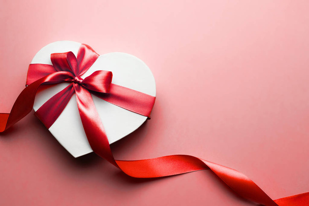 Kırmızı arka planda kırmızı kurdeleli kalp şeklinde bir kutu. Sevgililer Günü konsepti, yıldönümü, anneler günü ve doğum günü tebriği, telif alanı, üst görünüm. - Fotoğraf, Görsel