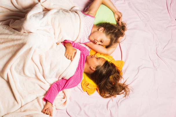 Kids in pink pajamas with messy hair covered with blanket - Фото, зображення