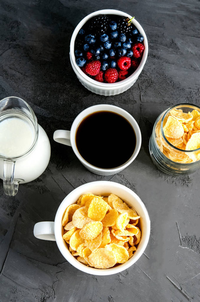 Healthy breakfast with cornflakes in a white cup, berries, milk and coffee on a dark gray background. - Fotoğraf, Görsel