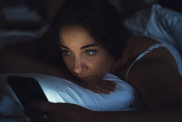 Woman uses smartphone in bed at night, close up - 写真・画像