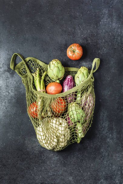 Fresh vegetables in a green string bag on a black background. Ca - Photo, image