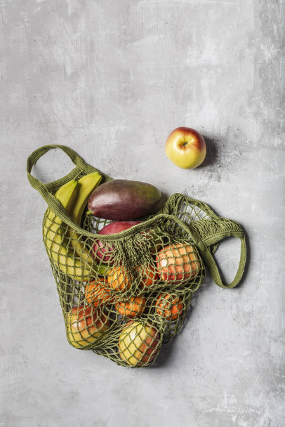 Fresh fruit in a green string bag on a light gray background. Ba - Zdjęcie, obraz