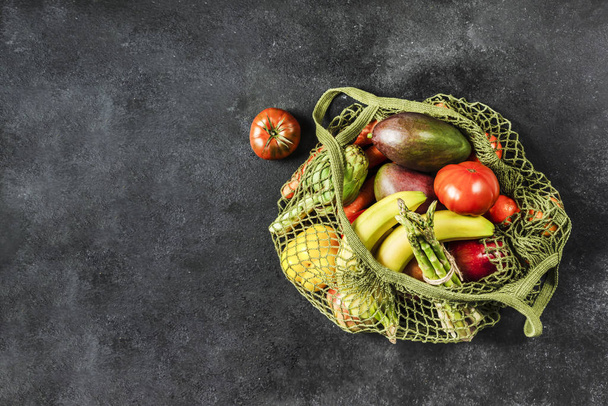 Fresh vegetables and fruits in a green string bag on a black bac - Foto, Bild