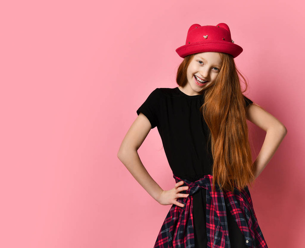 Teen female in black dress, checkered shirt on waist, red hat. She is laughing, hands on hips, posing on pink background. Close up - Foto, Bild