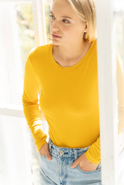 Calm beautiful girl in yellow sweater posing for camera at home - Foto, imagen