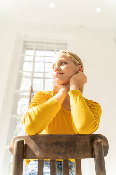 Calm smiling lady in yellow sweater sitting on chair against light background - Foto, Imagen