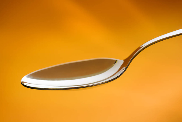 Empty metal spoon over a orange background - Фото, изображение