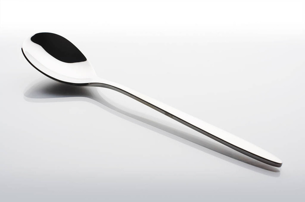 Small metal spoon over a white reflective background - Valokuva, kuva