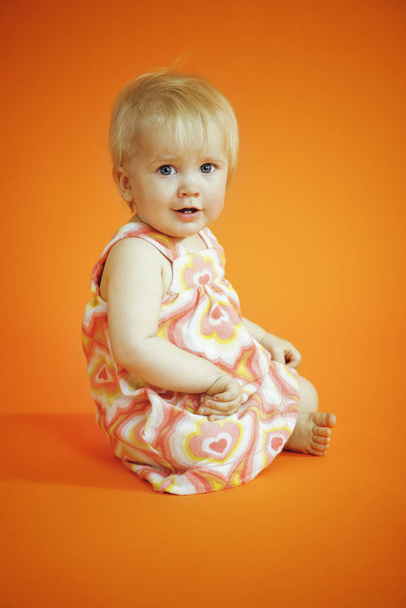 Small girl sitting on the orange background in studio - Fotografie, Obrázek