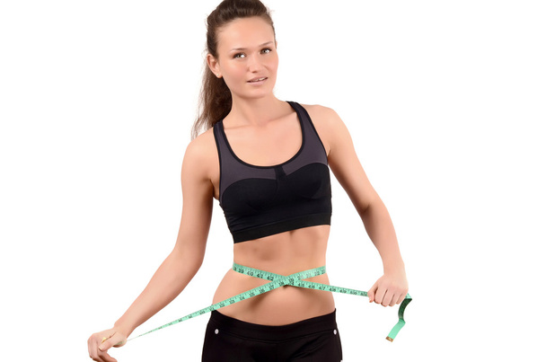 Beautiful fit girl measuring her waist with a green measuring tape in inch. - Foto, Imagen