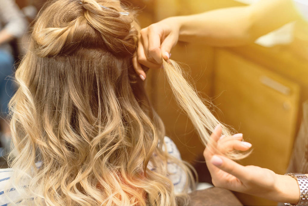 Fryzjer tworzy loki i falowane włosy w blondynce. Ręce loków fryzjerskich u klienta - Zdjęcie, obraz