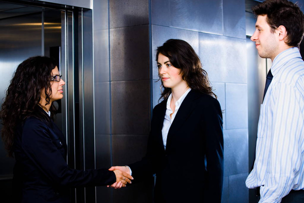 Smiling business people shaking hands at office lobby in front of elevator. - Fotó, kép