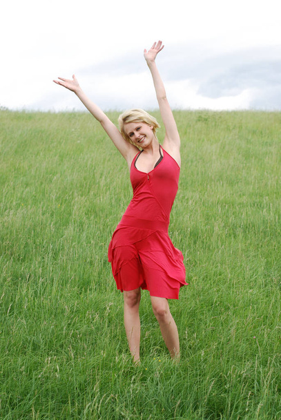 young woman in red dress jumping in field - Foto, Bild