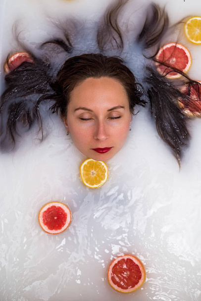 Young woman relaxing in a bath with milk and citrus fruits. - Fotó, kép