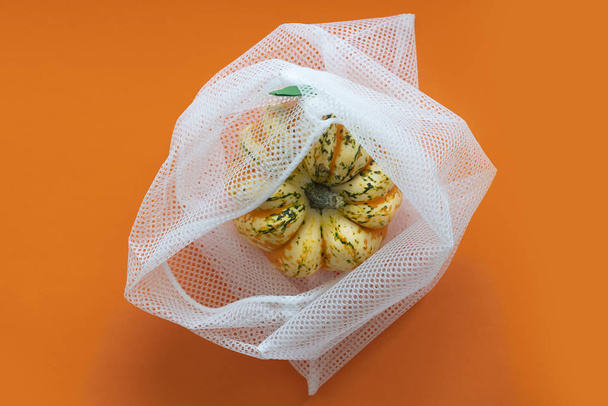 Pumpkin in a reusable mesh bag on orange background - zero waste concept - Photo, Image