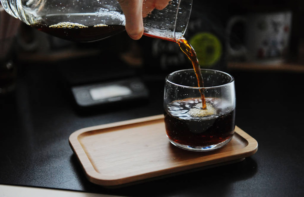Kézi főzés csendélet. Kávé öntése a kancsóból az üvegbe. Bambusztálca. Harmadik hullám sebességesztétika - Fotó, kép
