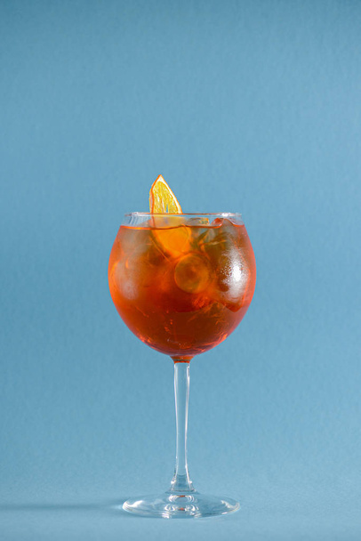 Red tropical alcohol cocktail with ice. Isolated on pastel blue background with copy space. Fruit cocktail in wine glass - Φωτογραφία, εικόνα