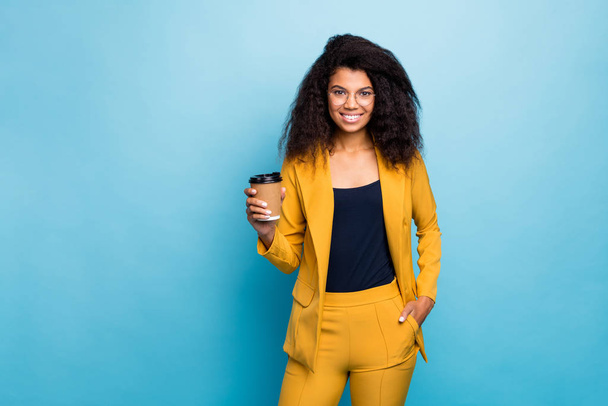 Photo of attractive chic dark skin wavy business lady holding hot takeout coffee beverage corporate dinner pause wear specs yellow suit blazer pants isolated blue color background - Photo, Image
