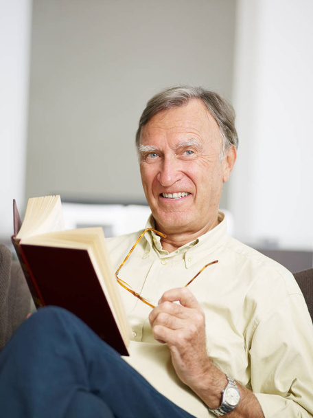 senior man reading book at home and looking at camera. Copy space - Фото, изображение