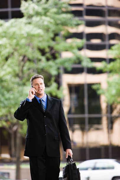Businessman walking outside and talking on his cell phone - Foto, imagen