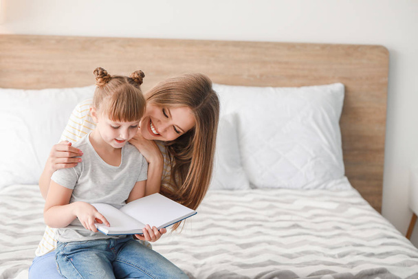 Beautiful young woman and her little daughter reading book at home - Фото, изображение