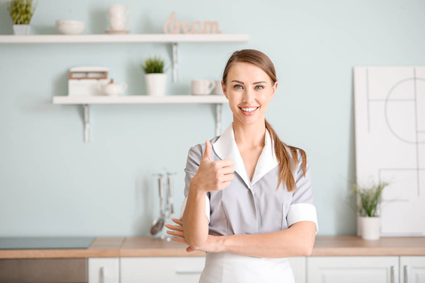 Retrato de hermosa camarera mostrando el pulgar hacia arriba en la cocina
 - Foto, imagen