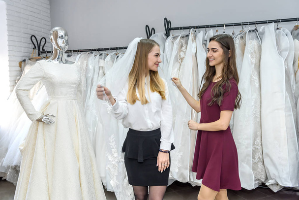 Saleswoman fitting veil for young bride in store - Foto, Bild