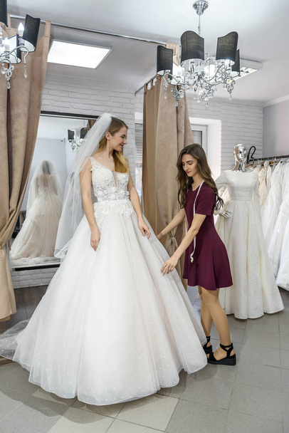 Tailor in wedding salon helping bride to try on  dress - Fotografie, Obrázek