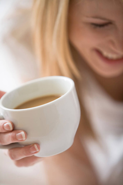 Partial face of woman holding up a white cup with coffee - Foto, imagen