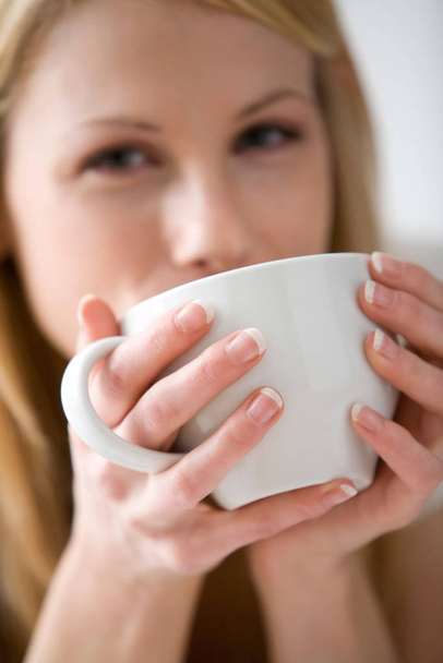 Blonde woman drinking from a white mug and looking at the camera - Foto, Imagen