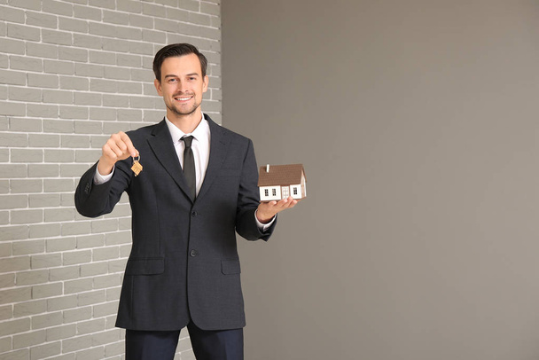 Retrato de agente inmobiliario masculino con llave y modelo de casa en el interior
 - Foto, Imagen