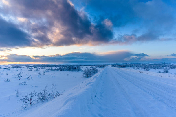 Winter Road coberto de neve com marcas de pneus ao pôr do sol
 - Foto, Imagem