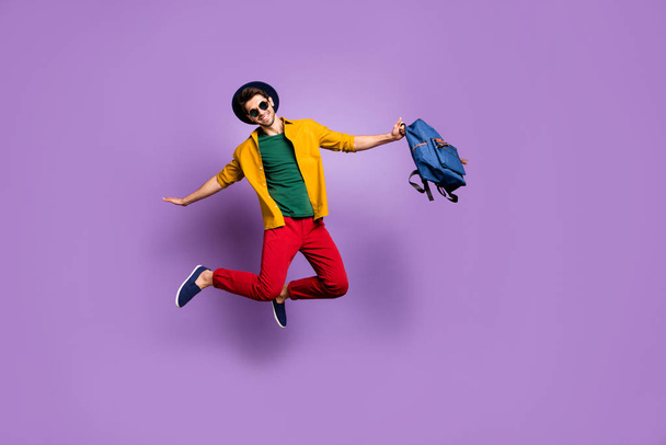 Full size photo of positive guy jump hold hands like bird fly hold blue backpack wear casual modern outfit isolated over purple color background - Фото, изображение