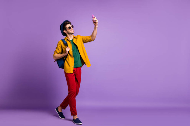 Full body profile side photo of positive guy tourist blogger go walk make selfie using smartphone wear modern casual style clothing over purple color background - Foto, imagen