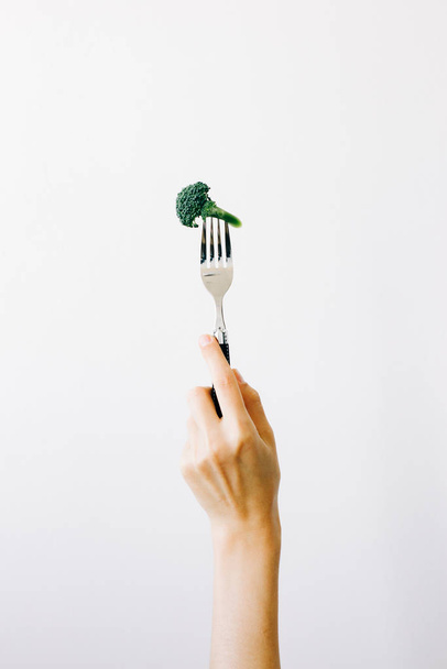 hand holding a fork with a green inflorescence of fresh broccoli on a white background. vegan food - Valokuva, kuva