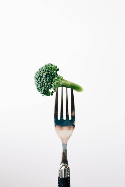 eine Gabel mit einem grünen Blütenstand aus frischem Brokkoli auf weißem Hintergrund. Veganes Essen - Foto, Bild