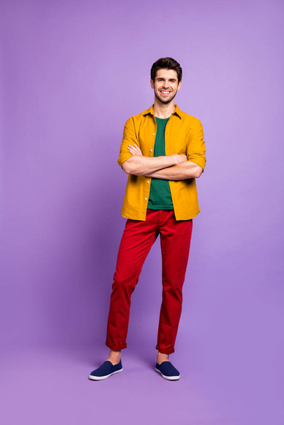Vertical Full length body size photo of toothy beaming handsome man in red pants footwear with arms crossed isolated violet pastel color background - Photo, image
